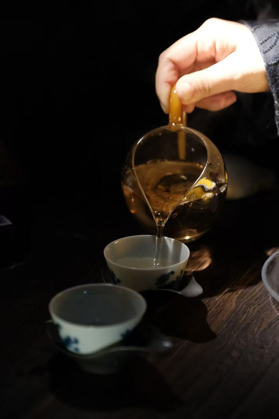 Tea host pouring from a glass pitcher in a dark tea room